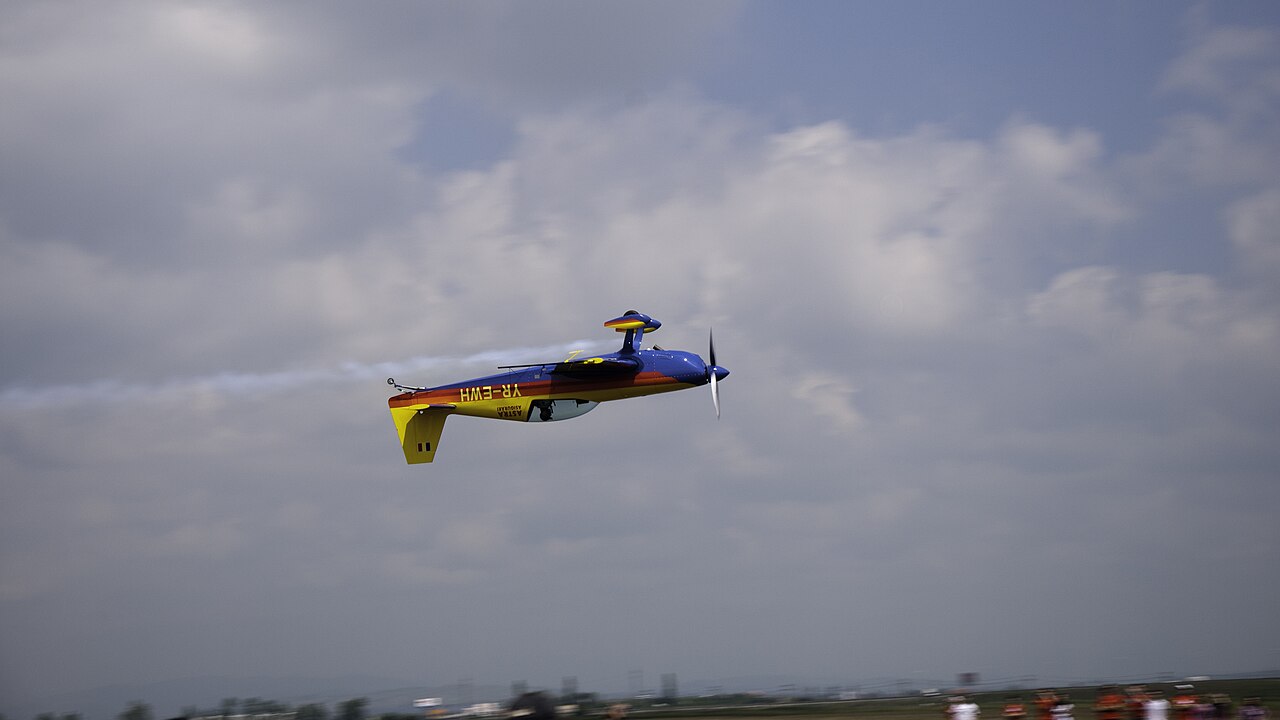 An Extra 300 aerobatic airplane flying upside down above an airshow field.