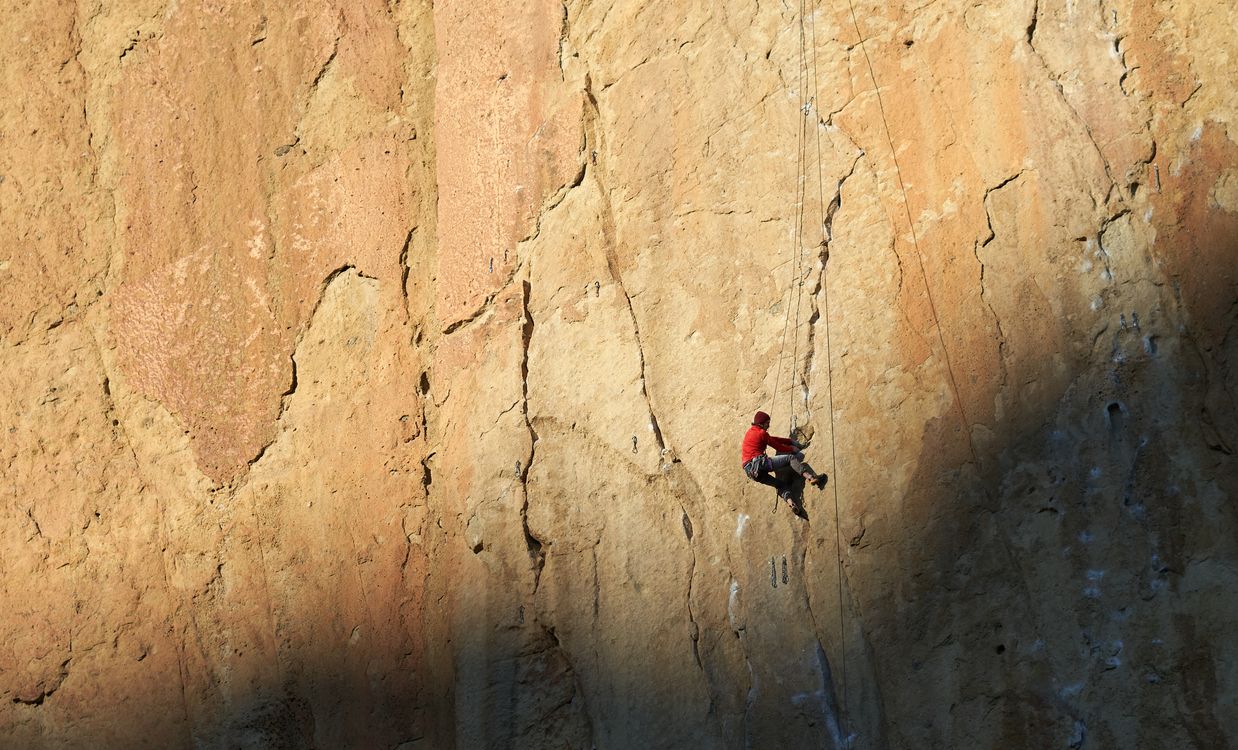 A climber in a red jacket ascending a rock face on a rope.