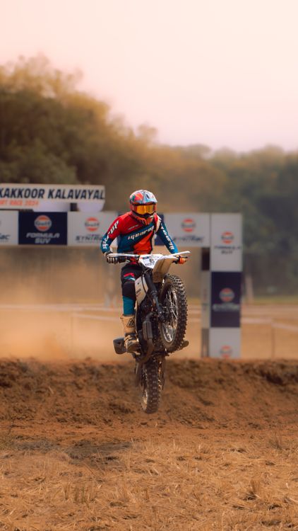 A helmeted motocross rider performing a wheelie on a dirt track.